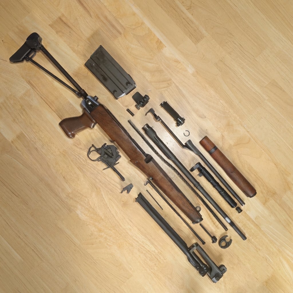 Disassembled rifle with a wooden stock and multiple metal components laid out on a light wood floor, including a detachable magazine and long barrel pieces, suggesting maintenance or repair work.