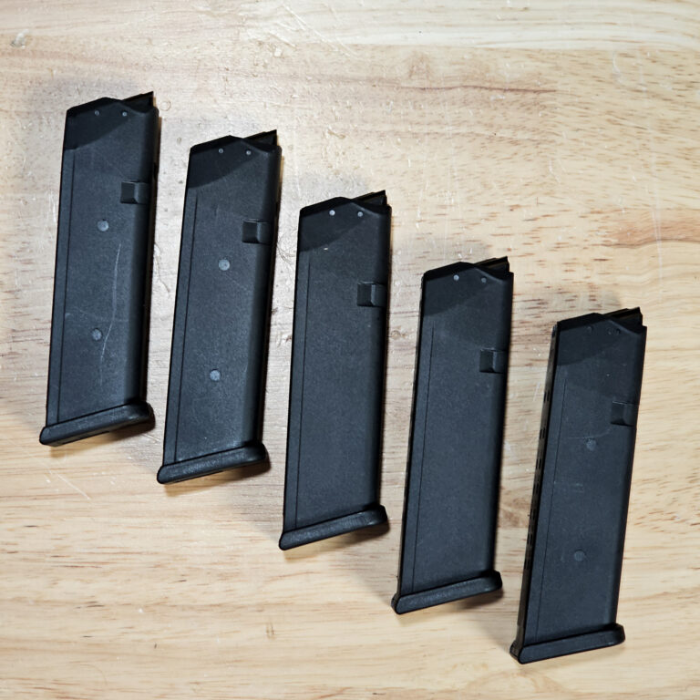 Several black rifle magazines arranged on a light wooden table surface.