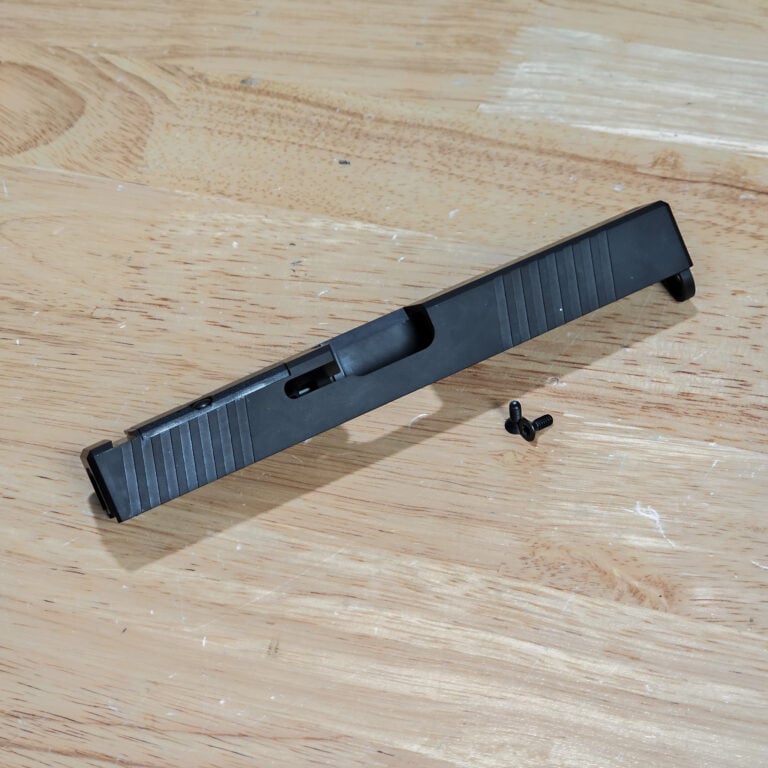 Close-up of a light wooden workbench with a black plastic component and a few loose screws nearby.